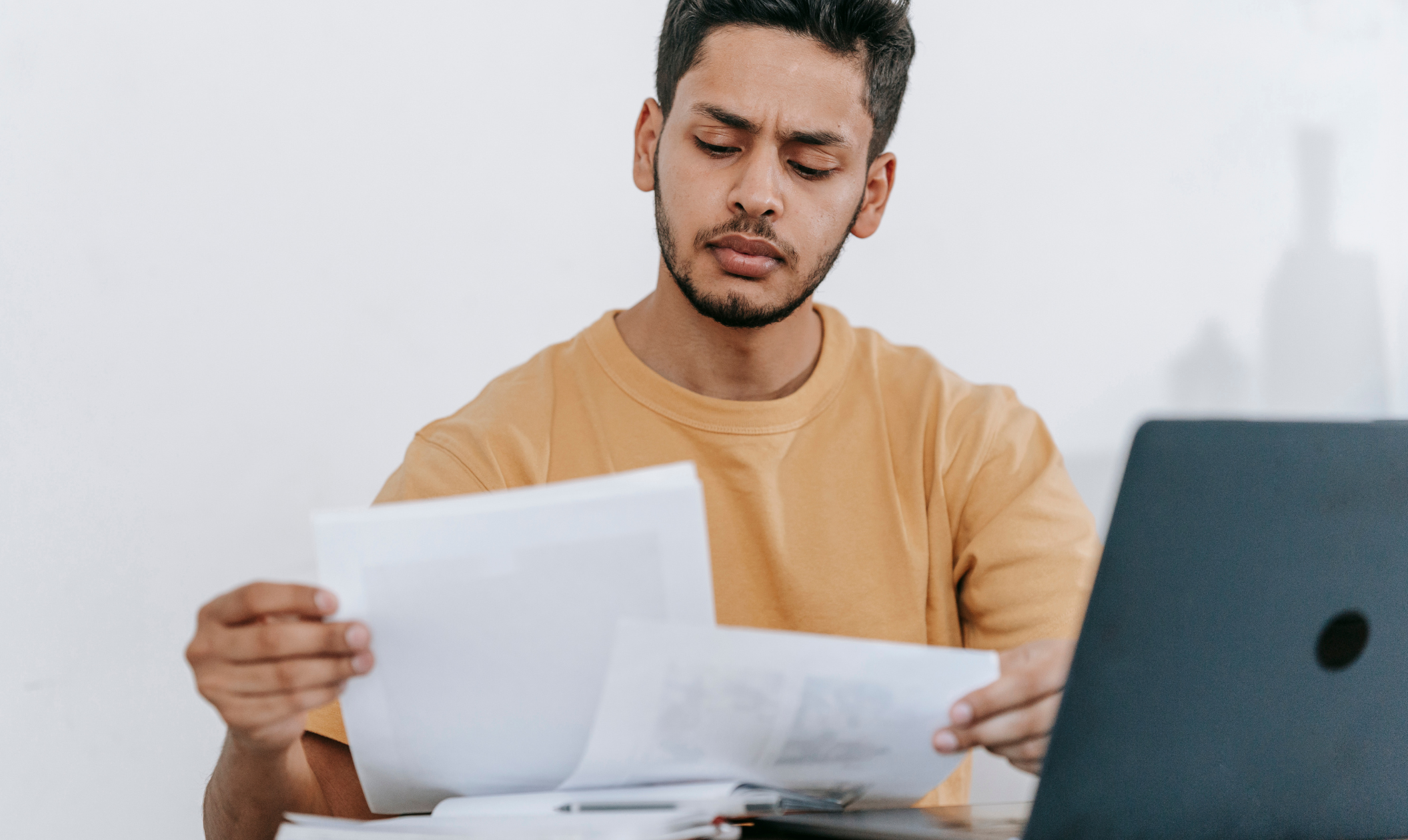 Man reviewing financial papers and laptop, checking for mistakes on credit report that could impact his score.