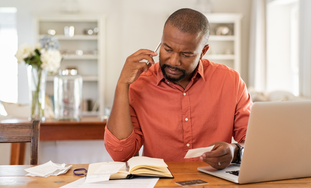 Man talking on the phone looking at laptop and receipts, calling to remove late payments from his credit report.