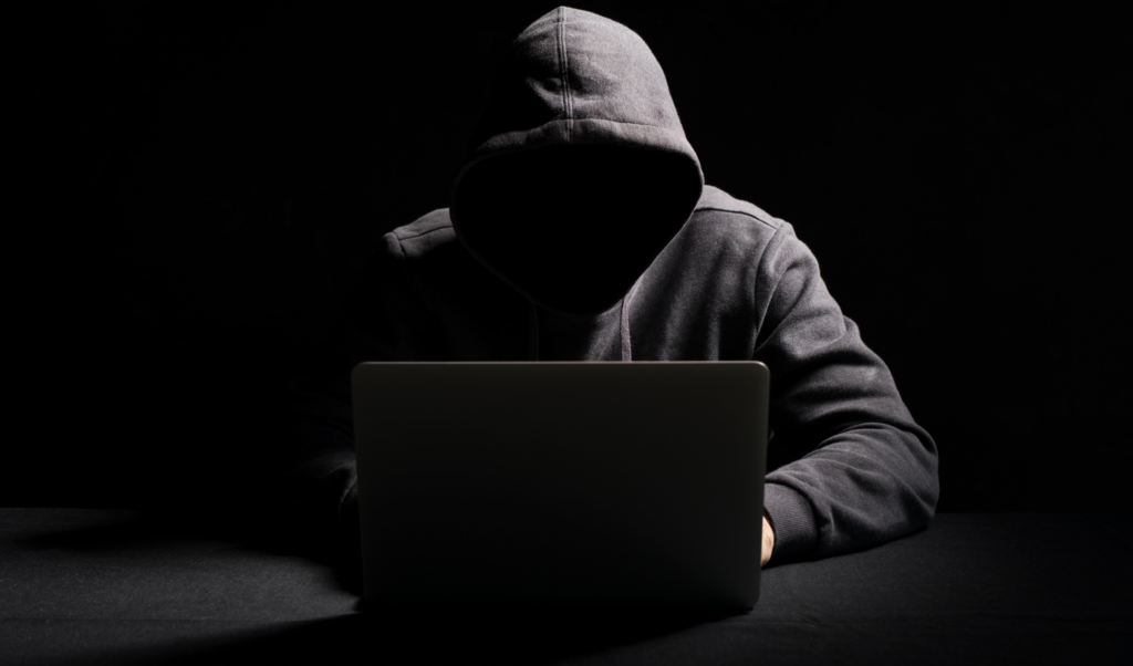 identity theft 2 - Consumer Law Professionals Hooded figure in shadows in front of a laptop to represent ghost students identity theft schemes.